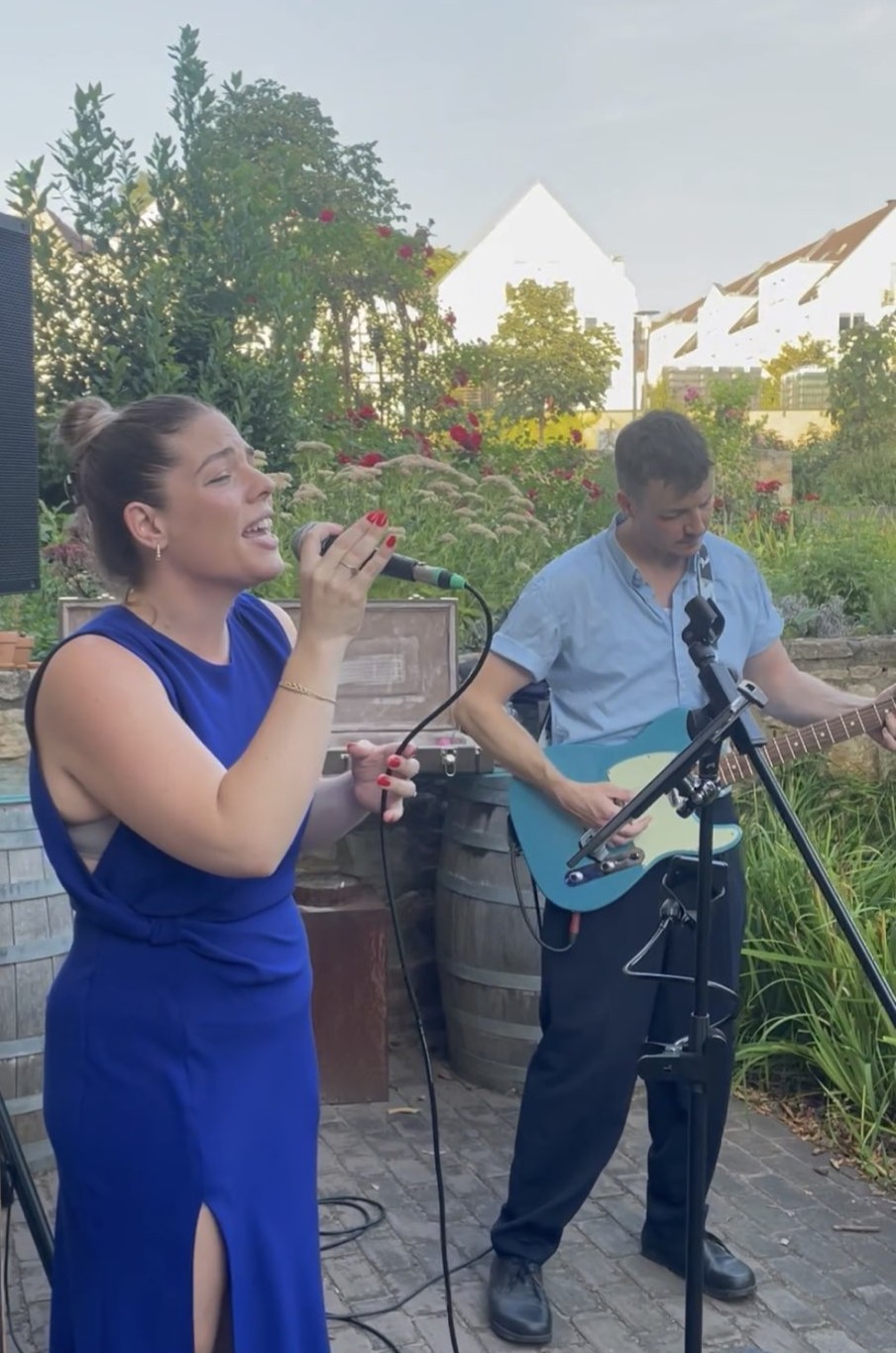 Brittany im blauen Kleid am Mikrofon, Diet an der blauen E-Gitarre, bei einem Abendauftritt im Garten