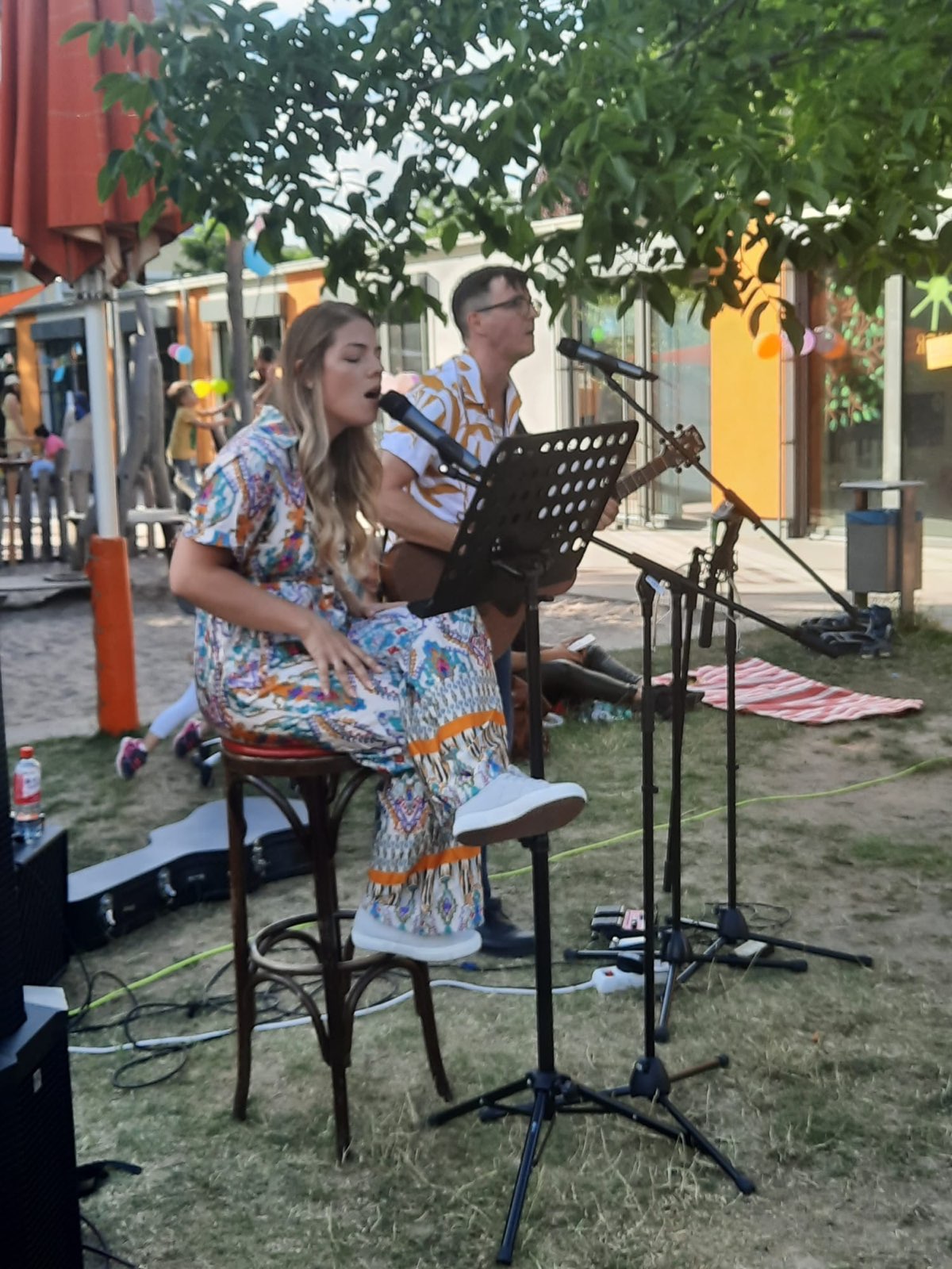 Brittany singt auf einem Barhocker, dahinter Diet an der Akustikgitarre, bei einem Open-Air-Auftritt