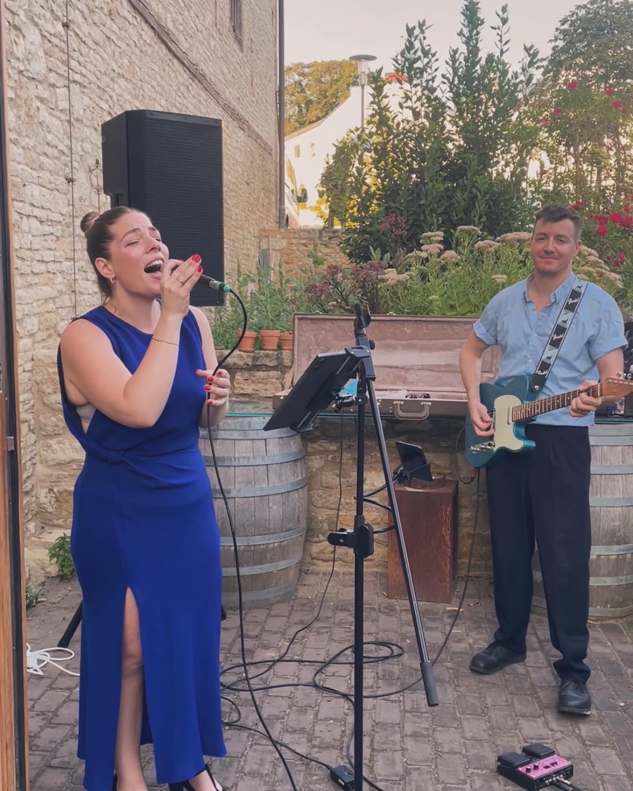 Brittany in a blue dress singing, Diet on electric guitar, at a garden wedding
